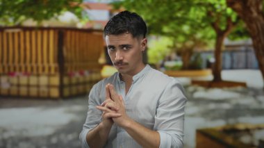 Ağaçlarla çevrili güneşli bir parkta el kol hareketleriyle silah taklit eden genç bir İspanyol.