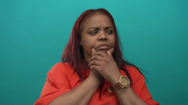 Kadın çeneye dokunur ve sonra stüdyoda turkuaz duvara parmak işareti yapar; merak.