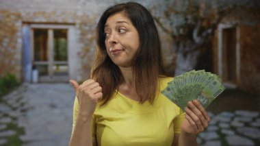 Orta yaşlı İspanyol kadın bir elinde peso banknotların hayranı, diğer elinde de ev girişinde baş parmak kaldırıyor..