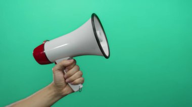Canlı yeşil arka plana karşı beyaz megafonu kavrayan erkek el iletişim ve duyuru öneriyor.