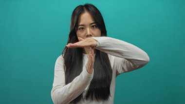 Asyalı bir kadın sağlam bir donuk zemine karşı zaman aşımı jesti yapıyor. Kırık eller odak noktasında duruyor, günlük beyaz bir gömlek giyiyor..