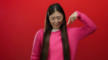 Pembe süveter giyen, uzun siyah saçlı, koyu kırmızı arka planda gülümseyen, aşağıya bakan, neşeli bir ifade ve canlı bir jest tasvir eden bir kadın..