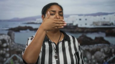 Çizgili üniforma giyen kadın hakem, deniz kenarı binası yakınlarındaki sokakta ellerini kaldırarak gözlerini kapatıyor; mahremiyet.