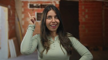 İnşaat alanında kapalı alanda gülümseyen bir kadın düşünceli ve yaratıcı bir şekilde el hareketleriyle bir fikir ya da içgörü sunuyor..