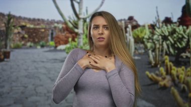 Açık hava parkında etrafı kaktüslerle çevrili bir kadın, güneşli bir günde yeşil bir çevrede duygusal bir an yakalıyor..