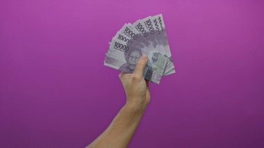 Kafkasyalı adam Endonezya rupia banknotlarını canlı pembe bir arka plana karşı tutuyor, izole edilmiş bir ortamda para gösteriyor..