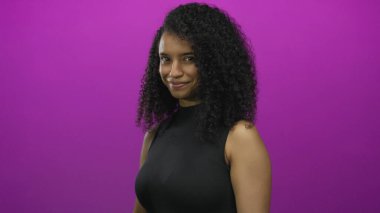 Genç, güler yüzlü, dost canlısı bir kadın pembe stüdyo duvarına parmak işareti yapar; davet.