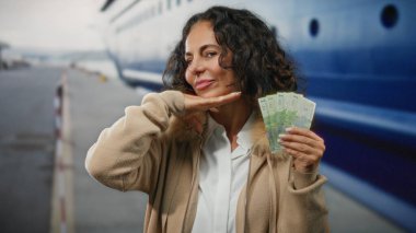 Orta yaşlı bir kadın arka planda teknesi olan bir sahil limanında Romanya banknotları tutuyor ve açık havada deniz kenarında rahat bir atmosfer yakalıyor..