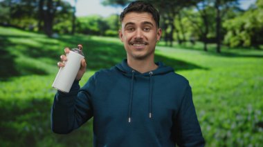 Güneşli bir günde parlak yeşil çimlerle dolu bir parkta sprey boya tutan genç İspanyol adam dışarıda rahat bir ortamda grafiti sanatıyla ilgili heyecanını dile getiriyor..