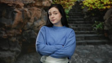 Kadın düşünceli bir şekilde bir parkta durmuş yeşil ışığın altında, taştan merdivenler ve yemyeşil bir yeşillik zeminine kurulmuş hayatı düşünerek, açık hava güzelliğini somutlaştırıyor..