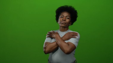 Yeşil arkaplana karşı güvenle poz veren kadın, minimalist stüdyoda gücünü somutlaştırıyor. Odaklanma ve güç, izole bir ifade ve tarzla gösteriliyor..