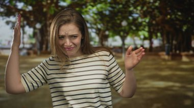 Çizgili tişörtlü kadın burnunu sıkar ve bir yaz öğleden sonra güneş ışığı altında elini kaldırır..