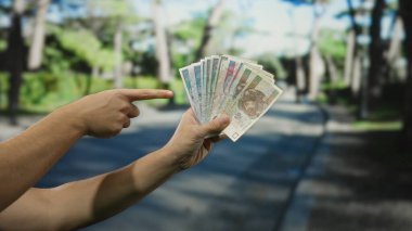 Bir şehrin caddesini işaret ederken elinde Polonya 'nın zloti banknotları tutan bir adam açık bir şehir ortamında para gösteriyor..