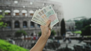 Erkek el, Roma Kolezyumu 'nun dışındaki hareketli şehir ortamında Czech Koruna banknotlarını tutuyor. Kültür ve para biriminin eşsiz bir karışımını yakalıyor..