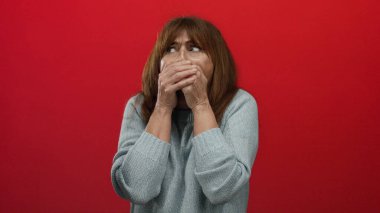 Geniş gözlü İspanyol son sınıf öğrencisi kadın koyu kırmızı bir duvara karşı ağzını kapatıyor. Gri bir kazak giyiyor. Mutlak zıtlık ortamında şaşkınlık ve şok hissi uyandırıyor..