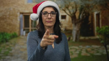 Noel Baba şapkası takan İspanyol kadın bina girişinde izleyiciye işaret ediyor; reddedilme.