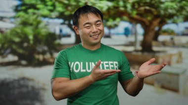 Yeşil gönüllü gömleğiyle gülümseyen genç adam güneşli parkta açık havada, bulanık ağaçlar ve banklarla çevrili, dost canlısı bir toplum atmosferini işaret ediyor..