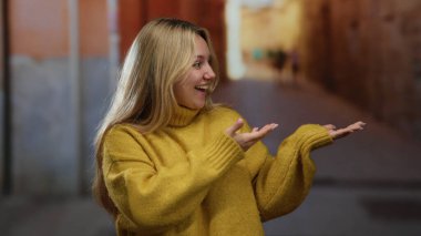 Sarı kazaklı kadın şehir caddesinde neşeli bir şekilde ellerini uzatıyor, gün ışığında canlı bir şehir manzarası sergiliyor, açık havada mutluluk ve pozitifliği ifade ediyor..