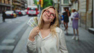 Gözlüklü, gülümseyen ve elinde Romanya parası olan genç bir kadın kalabalık bir şehir caddesinde zenginlik ve şehir yaşamını harmanlayan canlı bir sahne yaratıyor..