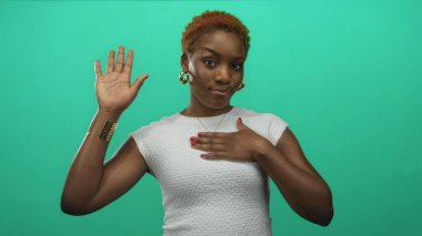 Nane yeşili stüdyoda el hareketi ve göğsünde altın halkalı küpeler olan ve sadakat yemini eden bir kadın..