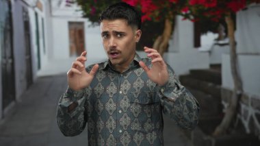 Beyaz binalar ve canlı çiçeklerle dolu bir caddede el kol gezen İspanyol genç adam şaşırmış görünüyor..