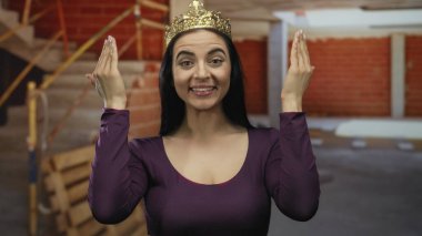 Taçlı İspanyol kadın, inşaat alanında kırmızı tuğlalı ve iç iskeleli komik suratlar yapıyor..