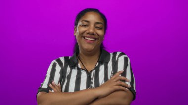 Hakem kadın, bir stüdyoda canlı mor bir arkaplan karşısında kollarını kavuşturarak güvenle gülümsüyor..