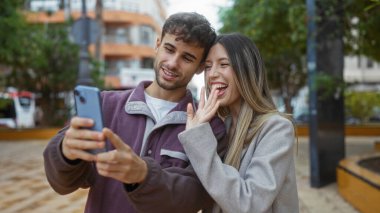 Şehir manzarasıyla çevrili şehir parkında neşeli bir video görüşmesi yapan, açık havada sevgi ve bağlantı sergileyen, ilişkilerini ve mutluluklarını vurgulayan bir çift..