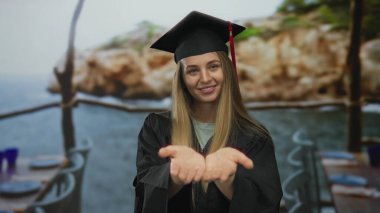 Şapkalı ve cüppeli bir kadın kayalık arka plan ve sakin deniz manzaralı manzaralı manzaralı bir plaj ortamında avuçlarını açıyor..