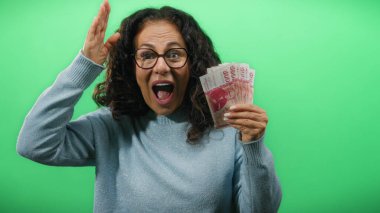 Icelandic Krona banknotları tutan orta yaşlı bir kadın canlı yeşil bir duvara bakıyor, merak ve heyecan taşıyor..