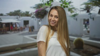 Güneşli bir avluda, yeşil ve beyaz mimarisi huzurlu bir ortamda gülümseyen bir kadın..