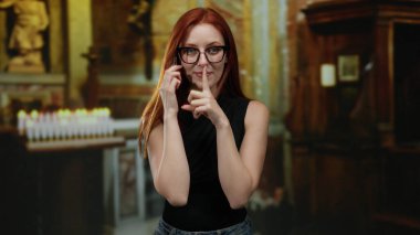 Genç, kızıl saçlı bir kadın kilise ortamında sessizliğe bürünüyor. Arka planda yanan mumlarla sağduyu ve sükunet taşıyor. Kapalı alan atmosferini yükseltiyor..