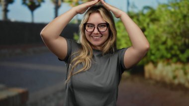 Gözlüklü gülümseyen kadın, güneşli bir günde şehrin arka planında elleri yukarıda, çatıda el sallıyor..