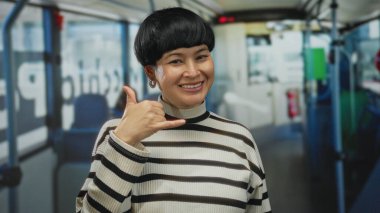 Otobüste çizgili süveter ve küpelerle el kol işareti yapan, neşeli, genç ve Çinli, kapalı alanda iletişim ve bağlantı kuran bir kadın..