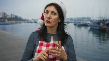 Noel Baba şapkalı kadın, limanda demirli bir gemi filosunun parmaklarını birbirine işaret ediyor..