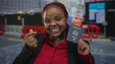 Kadın bize pasaport tutuyor ve şehir inşaatında gülümserken parmak kalp hareketi yapıyor; keyif yolculuğu.