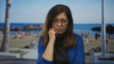 Mavi ceketli kadın, güneşli sahil sahilinde çenesi üzerinde oturur ve dalgalı sörf yapar..