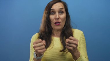 Sarı süveter içinde, izole edilmiş mavi arka planda kutlama yapan bir kadın.