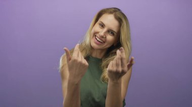 Mor arka planda el kol hareketi yapan, gülümseyen ve davetkar davranışları olan, sarı saçlı, yeşil elbiseli, stüdyoda izole edilmiş bir kadın..