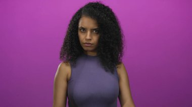 Kıvırcık saçlı genç İspanyol kadın parmak uçlarıyla stüdyoda pembe duvara doğru işaret ediyor..