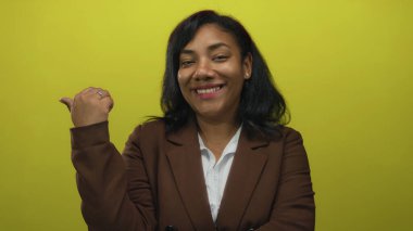 Sarı stüdyoda kahverengi ceketli ve beyaz gömlekli bir kadın parmak uçlarında geziyor..