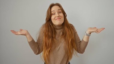 Beyaz arka plan üzerinde omuz silken, uzun kızıl saçlı, üstünkörü giyinen bir kadın stüdyo ortamında izole edilmiş kafa karışıklığını ifade ediyor.