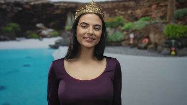 Bir havuz kenarında duran genç İspanyol kadın kayalık arka planda ve yemyeşil, açık havada zarafet ve gevşemeyi somutlaştıran bir tatil merkezinde..