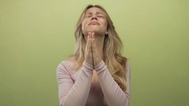 Avuç içleri katlanmış bir kadın stüdyo ortamında dua ederken umut dolu bir ifadeyle yukarıya bakıyor..