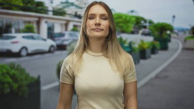 Kadın şehir caddesinde el kol hareketi yapıyor. Çevresi arabalar ve yeşilliklerle çevrili, şehir ortamında gelişigüzel etkileşimler sergiliyor..