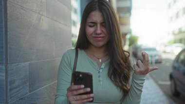 İspanyol kadın akıllı telefonu açık havada mutlu bir şekilde kullanıyor, neşe ve memnuniyeti ifade ediyor, teknolojiyle ilgileniyor..