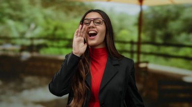 Genç İspanyol kadın yemyeşil bir açık hava parkında neşeyle bağırıyor, canlı enerji ve heyecanı vurguluyor..