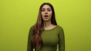 İzole edilmiş sarı arka plan duvarına karşı duran genç bir kadın tarafsız bir ifadeyle, sakinliği ve odaklanmayı somutlaştırıyor..