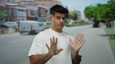 Beyaz gömlekli genç adam arka planda bulanık binalar ve araçlarla dolu kalabalık bir şehir caddesinde el kol hareketi yapıyor..