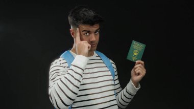 Elinde Çin pasaportu olan bir adam siyah arka planda kendine güvenen bir ifadeyle çizgili gömlek ve mavi sırt çantası takıyor.